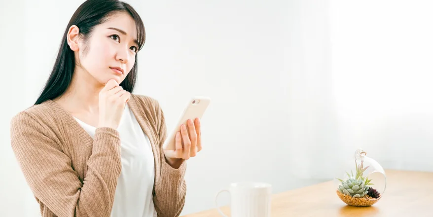 スマートフォンを片手に持ち、悩んでいる女性の様子