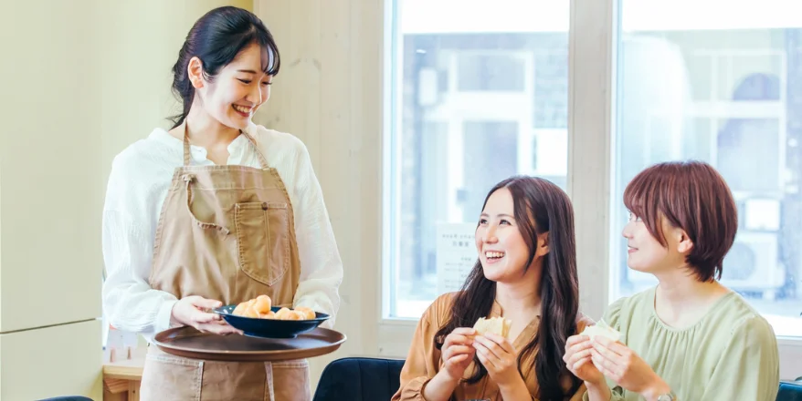 飲食店のスタッフが、お客様の女性2人に接客している様子